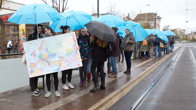 Junge Leute mit einer Europakarte und Europa-Regenschirmen stehen auf dem Bahnsteig