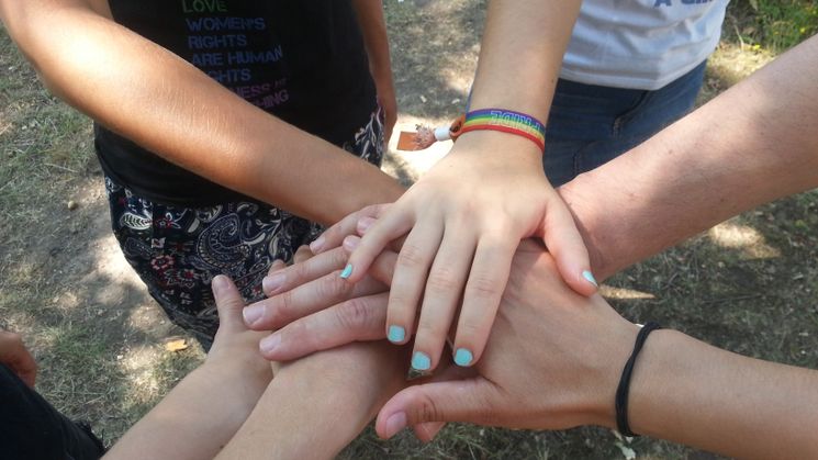 Sechs Jugendliche legen ihre Hände aufeinander. Eine junge Frau trägt ein Armband mit der Aufschrift PRIDE / Quelle: ©wir weit weg/KINDERVEREINIGUNG Leipzig e.V.