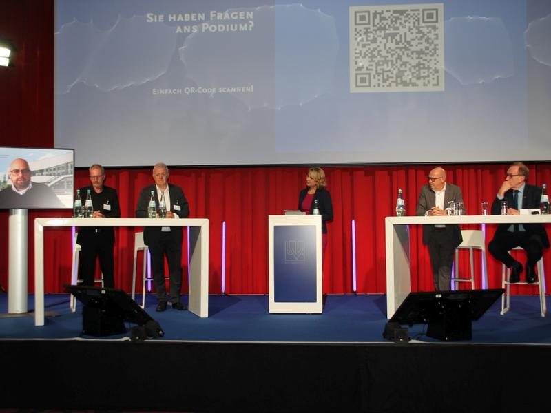 Das Diskussionspodium. Die Zuschauer hatten die Möglichkeit, über den QR-Code an der Projektionswand Fragen an die Podiumsteilnehmer zu stellen