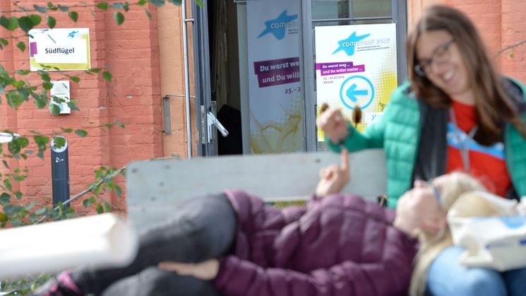 Zwei Frauen unterhalten sich vor dem Plakat "Du warst weg... Und du willst weiter"