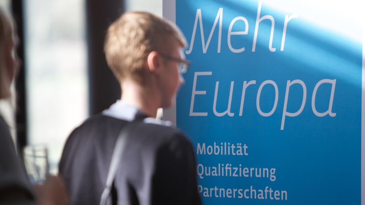 Ein junger Mann steht vor einem Banner mit der Aufschrift "Mehr Europa"