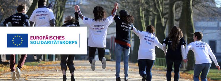 Junge Leute gehen Hand in Hand einen Straße entlang und tragen T-Shirts mit der Aufschrift Europäisches Solidaritätskorps