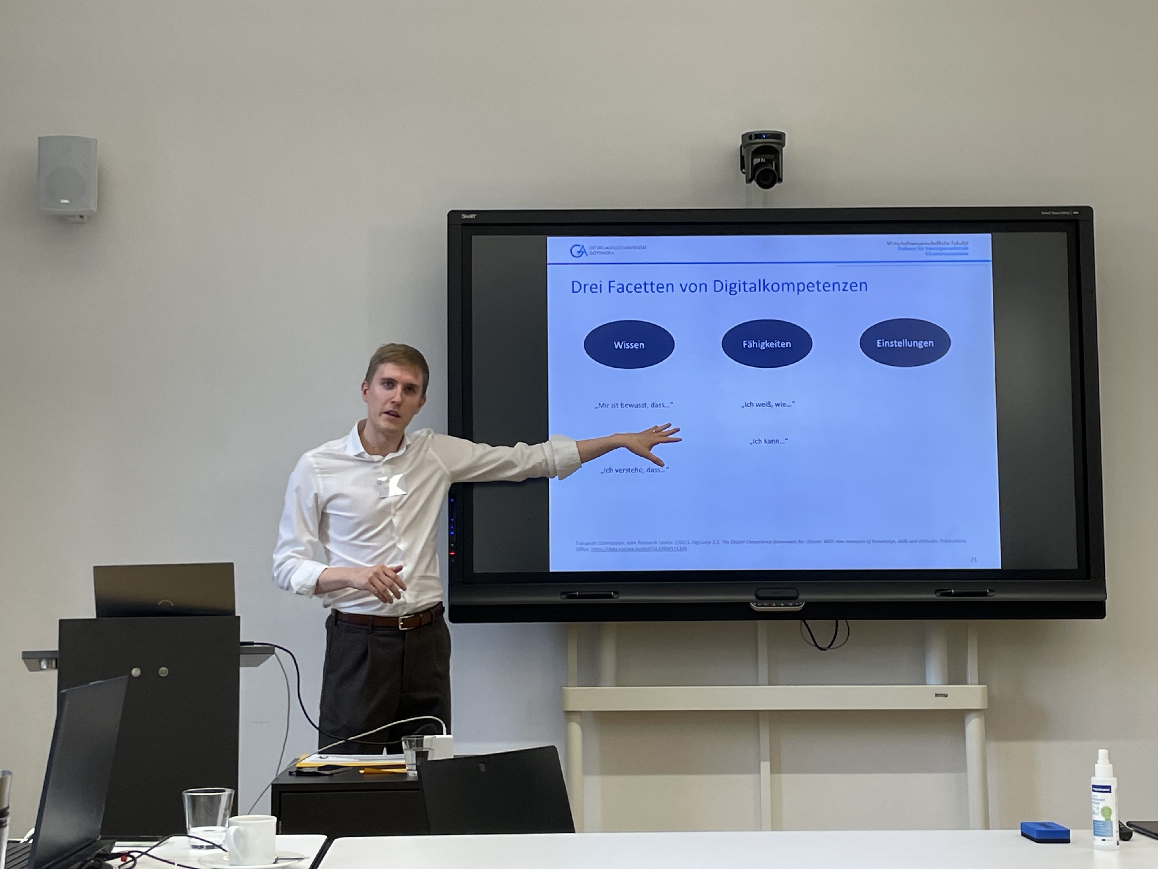 Mann zeigt sprechend auf großen Monitor.