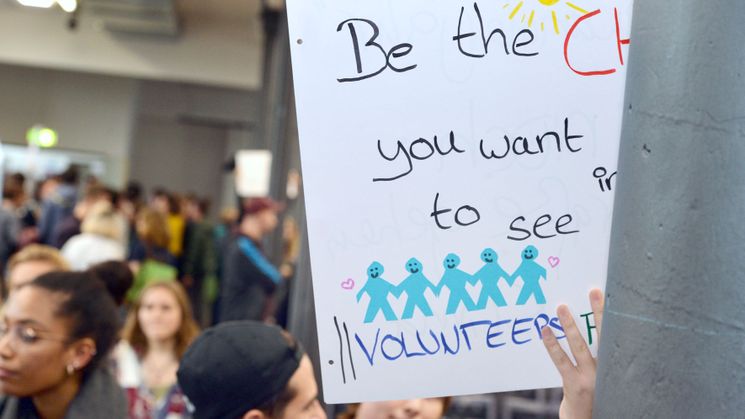 Freiwilliger hält Schild mit Aufschrift "Be the change you want to see" hoch